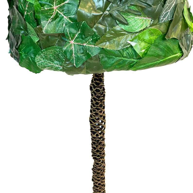 May include: A decorative topiary tree with a round, leafy crown made of green leaves. The trunk is wrapped in a textured, brown material. The leaves have a variety of green shades and some have pink veins.