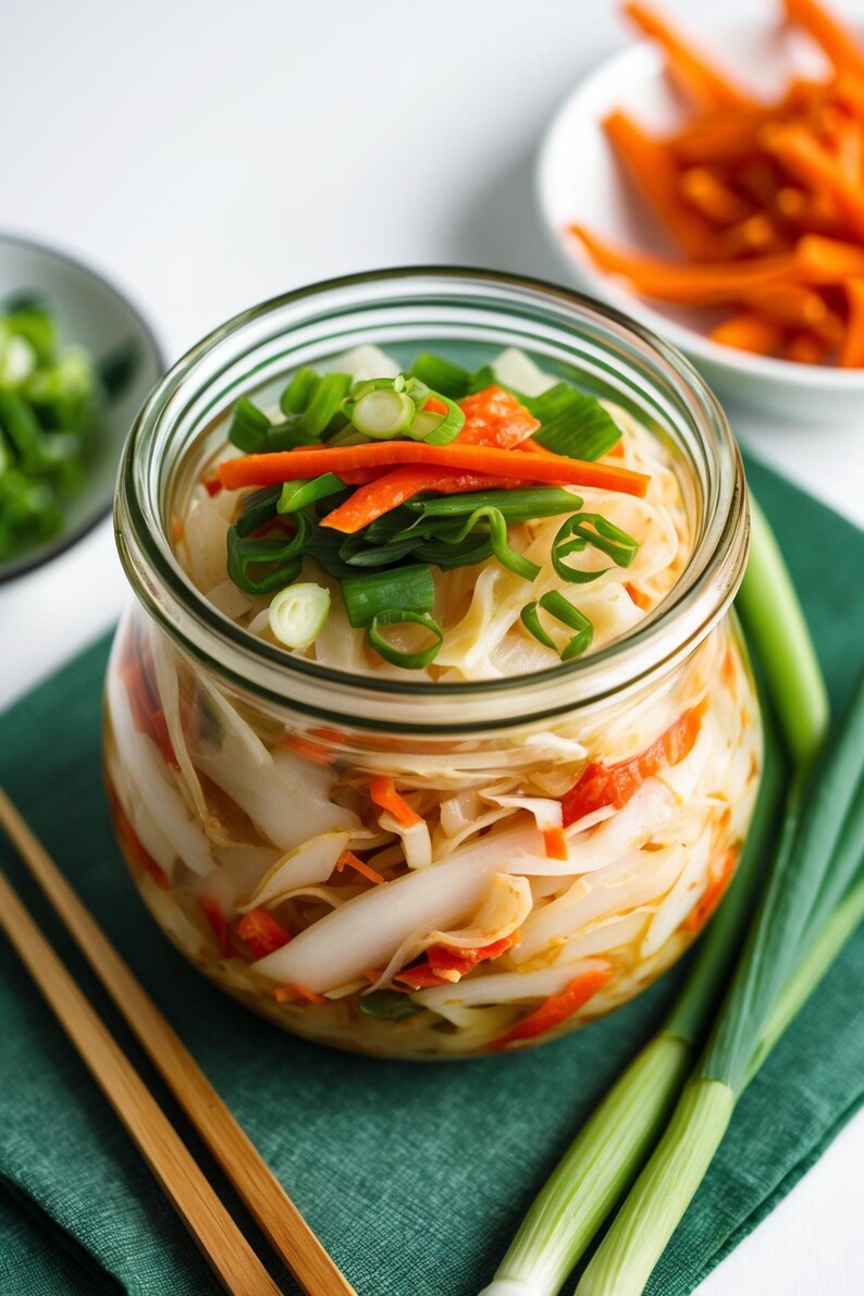 K&ouml;nnte beinhalten: Ein Glas mit Kimchi, einer traditionellen koreanischen Beilage. Das Kimchi besteht aus wei&szlig;em Kohl, orangefarbenen Karotten und gr&uuml;nen Fr&uuml;hlingszwiebeln. Zus&auml;tzliche Fr&uuml;hlingszwiebeln und Karotten befinden sich in kleinen Schalen.