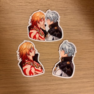 以下が含まれることがあります： 2人のキャラクターのアニメ風イラストが描かれた3つのステッカー。1人はオレンジ色の髪と赤い模様、もう1人は青い髪をしています。ステッカーは木製の表面にあります。