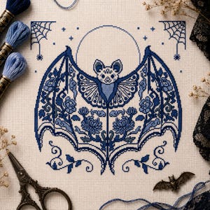Può includere: Un motivo a punto croce su tessuto color crema raffigurante un pipistrello centrale con le ali spiegate, decorato con intricati motivi floreali e geometrici blu. Una grande luna circolare si trova dietro il pipistrello.