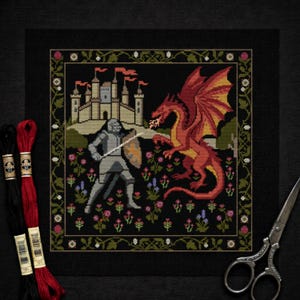 May include: Cross-stitch showing a knight fighting a red dragon before a castle. The scene is framed by a floral border on a black background. Embroidery threads and scissors are visible.