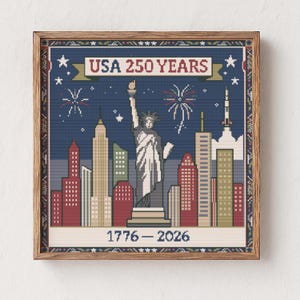 May include: Framed cross-stitch art featuring the Statue of Liberty and a cityscape with fireworks against a navy blue background. The banner reads "USA 250 YEARS" with the years "1776-2026" below. The artwork is in a wooden frame.