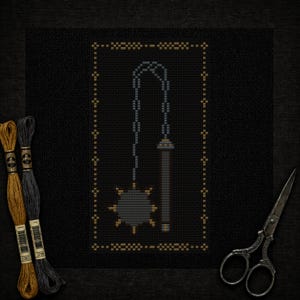 May include: Cross-stitch design of a mace with a spiked ball and chain, framed in gold on black fabric. Includes gold and gray embroidery floss and vintage scissors.