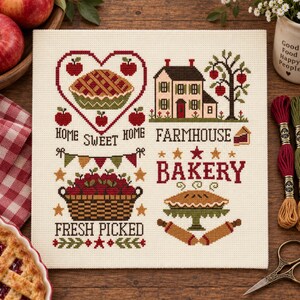 Può includere: Un ricamo a punto croce su tessuto color crema raffigurante una torta a forma di cuore, una fattoria, un cesto di mele rosse e una torta su un'alzata. Il testo include HOME SWEET HOME, FARMHOUSE BAKERY e FRESH PICKED, con stelle e festoni.