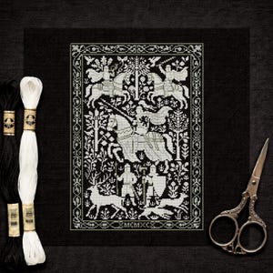 May include: Black and white cross-stitch embroidery featuring a medieval scene with knights on horseback, deer, and figures. The design is framed with a decorative border. Embroidery floss and scissors are next to the cross-stitch.