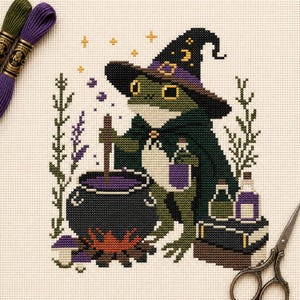 Puede incluir: Un patrón de punto de cruz sobre tela blanca que muestra una rana verde con sombrero de bruja y capa negra. La rana remueve un caldero negro con líquido morado sobre un fuego. Cerca hay frascos de pociones, un libro y ramas de lavanda.