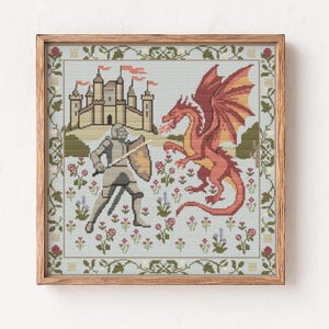 May include: Cross-stitch artwork in a wooden frame depicts a knight facing a red dragon near a castle. The knight holds a sword and shield, while the dragon breathes fire. The background features a light blue sky and a floral border.