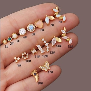Può includere: Una collezione di orecchini dorati con vari design, tra cui borchie, grappoli e pendenti. Gli orecchini presentano pietre preziose, opali e accenti di cristallo. Gli stili includono forme floreali, a cuore, a farfalla e geometriche.