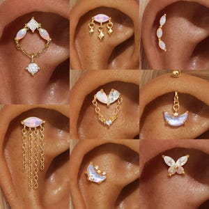 May include: A collection of gold-toned earrings with opalescent and clear crystal accents. Designs include a chain with a diamond-shaped pendant, a dangling teardrop design, and a butterfly shape. The earrings are shown on an ear.