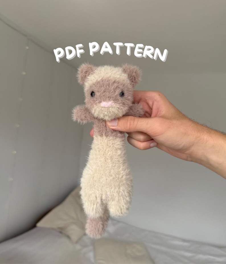 May include: A handmade plush ferret toy in shades of beige and mauve, held up against a white background. The ferret has a fluffy texture, small ears, and a pink nose. The text "PDF PATTERN" is displayed above the toy.