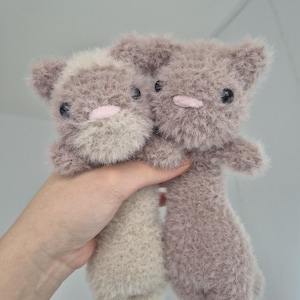 May include: Two handmade plush cat toys. The toys are a soft, fuzzy material in shades of gray and beige. Each cat has black button eyes and a pink nose. The toys are held up against a plain background.