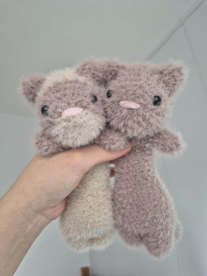 May include: Two handmade plush cat toys. The toys are a soft, fuzzy material in shades of gray and beige. Each cat has black button eyes and a pink nose. The toys are held up against a plain background.