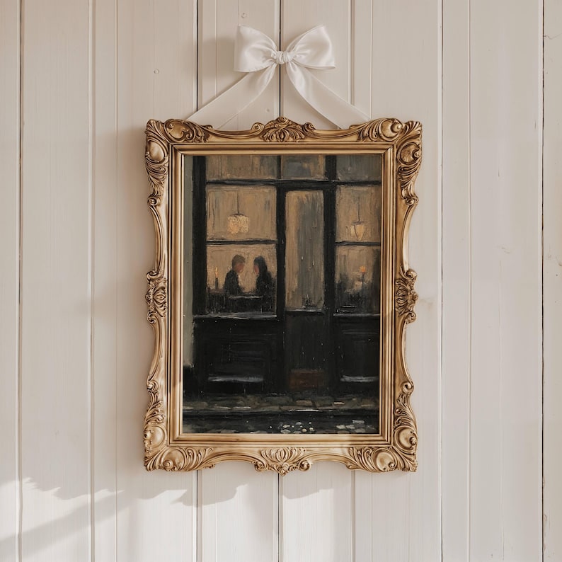 May include: A rectangular painting in an ornate gold frame featuring a dark, moody scene of two figures sitting inside a dimly lit cafe storefront. A large, white satin ribbon bow is attached to the top centre of the frame for hanging.