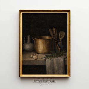 May include: A framed wall art print titled COTTAGE LANE PRINTS featuring a still life painting of a brass pot, a ceramic pitcher, wooden kitchen utensils, two small onions, and a sprig of green herbs resting on a cloth-covered table surface.