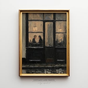 May include: A framed oil painting print depicting a dark storefront at night with two figures sitting inside by warm light. The scene features a cobblestone street in the foreground, large window panes, and a gold-coloured frame. Text reads COTTAGE LANE PRINTS.