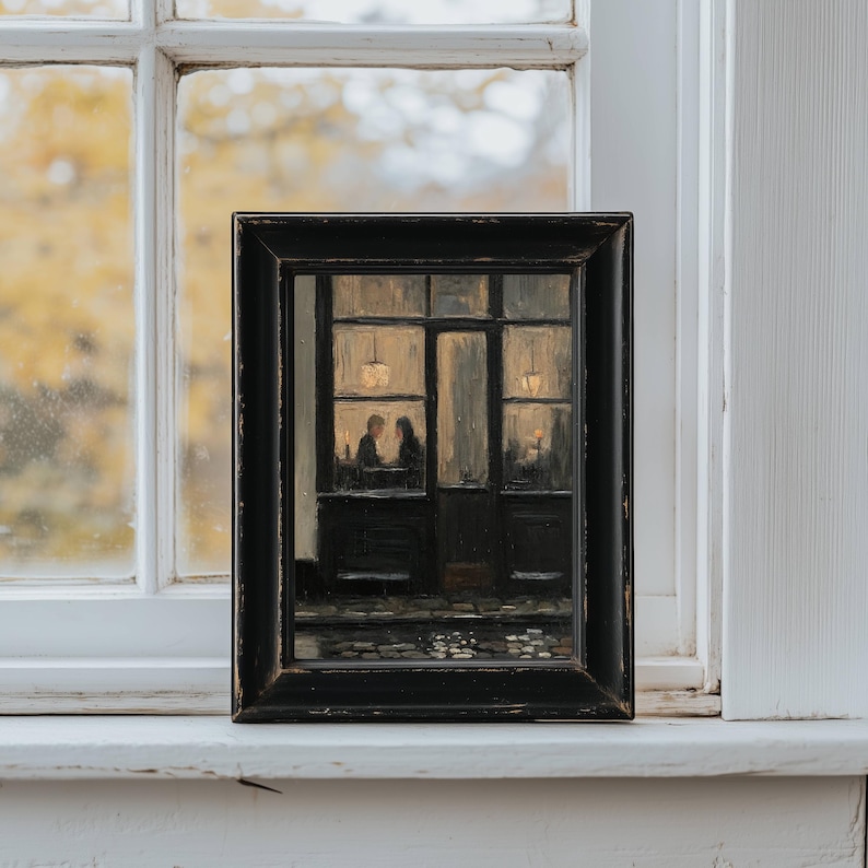 May include: A framed oil painting depicting a dark, moody street scene at night. The artwork shows a storefront with large windows, illuminated by warm interior lights, where two figures are seated at a table. The frame is black and rectangular.