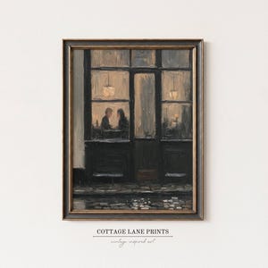 May include: A framed oil painting print depicting a dark storefront at night with two figures seated inside under warm glowing lights. The scene features a cobblestone street in the foreground and the text COTTAGE LANE PRINTS at the bottom.
