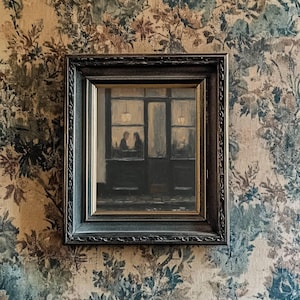 May include: A framed oil painting depicting a dark storefront exterior at night with two figures visible through the window glass. The artwork is encased in a dark, ornate, textured frame with gold inner trim, hanging on a floral patterned wall.
