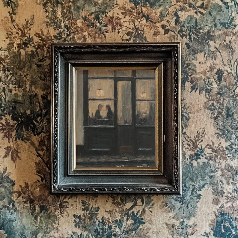 May include: A framed oil painting depicting a dark storefront exterior at night with two figures visible through the window glass. The artwork is encased in a dark, ornate, textured frame with gold inner trim, hanging on a floral patterned wall.
