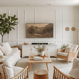 May include: A bright, airy living room with white paneling, a light-colored rug, and a wooden coffee table. Two rattan armchairs and a white sofa are arranged around the table. A large landscape painting hangs above a white cabinet.