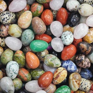 May include: A selection of polished gemstone eggs in a variety of colours and patterns. The collection includes eggs in shades of pink, green, red, black, white, and speckled designs. These decorative eggs are suitable for display or collection.