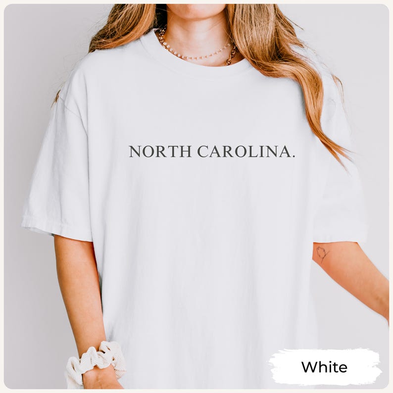 May include: White t-shirt with the text "NORTH CAROLINA." printed in a simple, dark font across the chest. The shirt is a solid white colour and has short sleeves. The word "White" is in a white rectangle in the bottom right corner.
