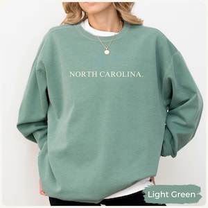 May include: Light green sweatshirt with the text "NORTH CAROLINA." in white. The sweatshirt has long sleeves and a crew neck. The bottom right corner of the image has the text "Light Green."