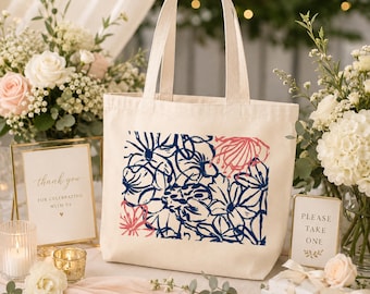 May include: A cream-colored canvas tote bag featuring a rectangular graphic print of stylized flowers in navy blue and coral pink. The bag has two matching fabric handles and a rectangular base, showcasing a clean, simple design for daily use.