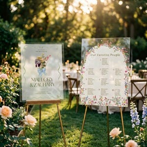 May include: Two clear acrylic wedding signs on gold stands. The left sign features a floral bouquet illustration and the text Mallory & Zachary. The right sign is titled Our Favorite People and lists guest names under ten numbered table categories.