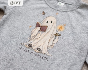 May include: A heather grey long-sleeve shirt featuring a graphic of a ghost wearing black sneakers, reading a book, and holding a lit candle. The text "MOSTLY HARMLESS." is printed below the ghost, accompanied by small star and moth illustrations.