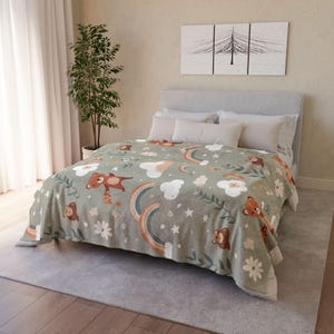 Op de afbeelding: Een saliegroene deken met een herhalend patroon van bruine teddyberen, regenbogen, witte wolken en bloemen. De deken ligt op een bed met witte kussens en een grijs hoofdbord. De deken is gemaakt van zacht materiaal.