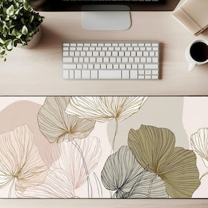 May include: A rectangular desk mat featuring a floral design in neutral tones. The mat showcases stylized flowers in shades of beige, olive green, and gold, with delicate line art details. The background has soft, abstract shapes in blush and beige.