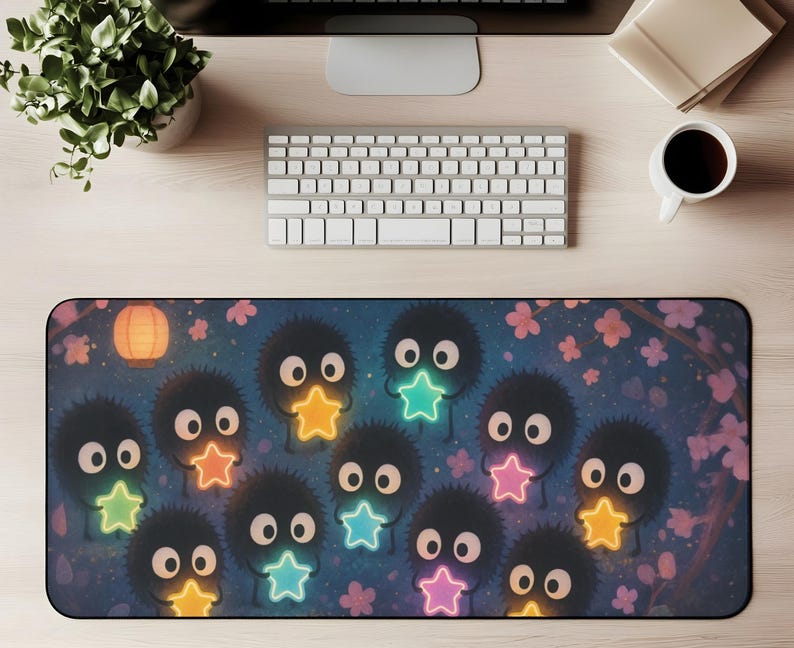 May include: A rectangular desk mat featuring a whimsical design with cartoon-like creatures holding glowing star shapes. The mat has a dark blue background with pink floral accents and a paper lantern.