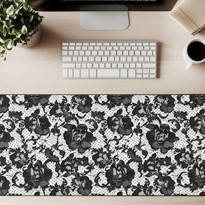 May include: Black and white desk mat featuring a floral lace pattern. The design includes large, detailed black roses and other floral elements against a white background. The mat is rectangular and designed to fit under a keyboard and mouse.