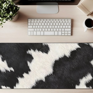 Pode incluir: Tapete de mesa retangular com um padrão de pele de vaca em preto e branco. O tapete foi projetado para proteger a superfície da mesa e fornecer uma área lisa para um mouse e teclado. O tapete tem uma borda preta.