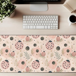 May include: A rectangular desk mat featuring a repeating pattern of pink ladybugs with black spots, dark green leaves, and dark gray circles on a light beige background. The mat is designed to protect a desk surface.