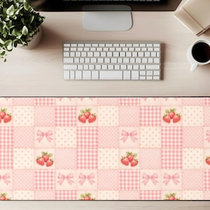 May include: A rectangular desk mat featuring a patchwork design in shades of pink and cream. The pattern includes squares with strawberries, bows, and gingham and polka dot patterns. The mat is designed to protect a desk surface.