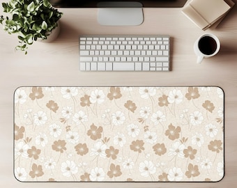 Puede incluir: Alfombrilla de escritorio rectangular con un estampado floral. La alfombrilla presenta un fondo beige con un diseño repetido de flores blancas y marrones. La alfombrilla está rodeada por un borde negro y está diseñada para proteger la superficie del escritorio.