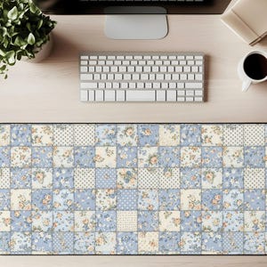 May include: A rectangular desk mat with a patchwork design. The mat features a pattern of squares in light blue, cream, and white, with floral and polka dot motifs. The mat is designed to protect a desk surface.