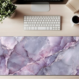 May include: A rectangular desk mat with a marble design in shades of purple, gray, and white. The mat features a smooth surface and is designed to protect the desk from scratches. It is a decorative and functional accessory for a workspace.