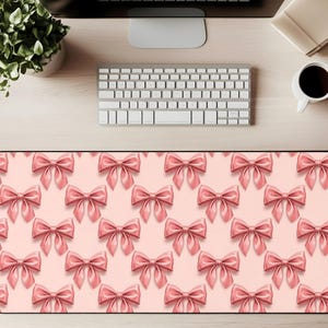 Puede incluir: Alfombrilla de ratón rectangular con un patrón repetido de lazos rosas sobre un fondo rosa claro. Los lazos tienen una apariencia brillante y tridimensional. La alfombrilla está diseñada para colocarse debajo de un teclado y un ratón.