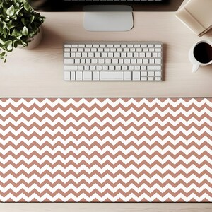 May include: A rectangular desk mat with a repeating chevron pattern in white and a muted reddish-brown color. The mat is designed to protect a desk surface and provide a smooth area for a mouse and keyboard.