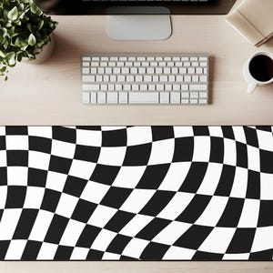May include: Black and white checkered pattern desk mat. The mat has a wavy design and is rectangular. A keyboard, computer monitor, and coffee cup are visible in the background.