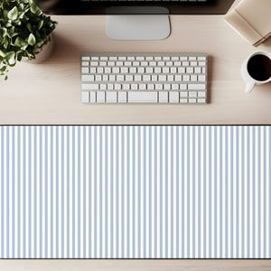 May include: A rectangular desk mat with a pattern of vertical blue and white stripes. The mat is on a light wood surface, with a keyboard, coffee cup, and plant visible.