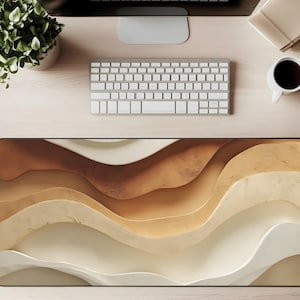 May include: A rectangular desk mat with a wavy, abstract design in shades of brown, beige, and white. The mat is placed on a light wood desk, with a keyboard, monitor, coffee cup, and plant visible.