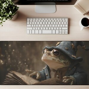 May include: A whimsical mousepad featuring a frog dressed as a wizard, wearing a blue hat with gold stars and a blue coat. The frog is reading a spell book, with magical sparkles in the background. The mousepad is rectangular and black.