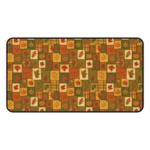 Op de afbeelding: Rechthoekige mat met een patchwork ontwerp met herfstbladeren en pompoenen in tinten oranje, geel en groen. De vierkanten hebben verschillende patronen, waaronder ruitjes en stippen, met een zwarte rand.