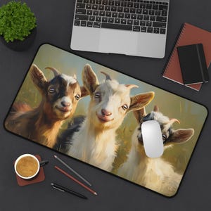 May include: A rectangular mouse mat with a cheerful illustration of three goats smiling. The goats have brown, white, and black fur, set against a grassy field. A laptop, notebook, and a coffee cup are also visible.