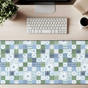 May include: A rectangular desk mat with a patchwork design in shades of blue and green. The pattern includes floral and plaid squares. The mat is designed to protect the desk surface and provide a smooth area for a mouse and keyboard.