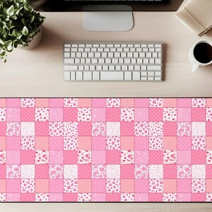Puede incluir: Alfombrilla de escritorio rectangular con un diseño de patchwork en tonos rosa y blanco. El patrón presenta cuadrados con motivos florales, de lunares y paisley. La alfombrilla está diseñada para proteger la superficie del escritorio y proporcionar un área lisa para el ratón y el teclado.